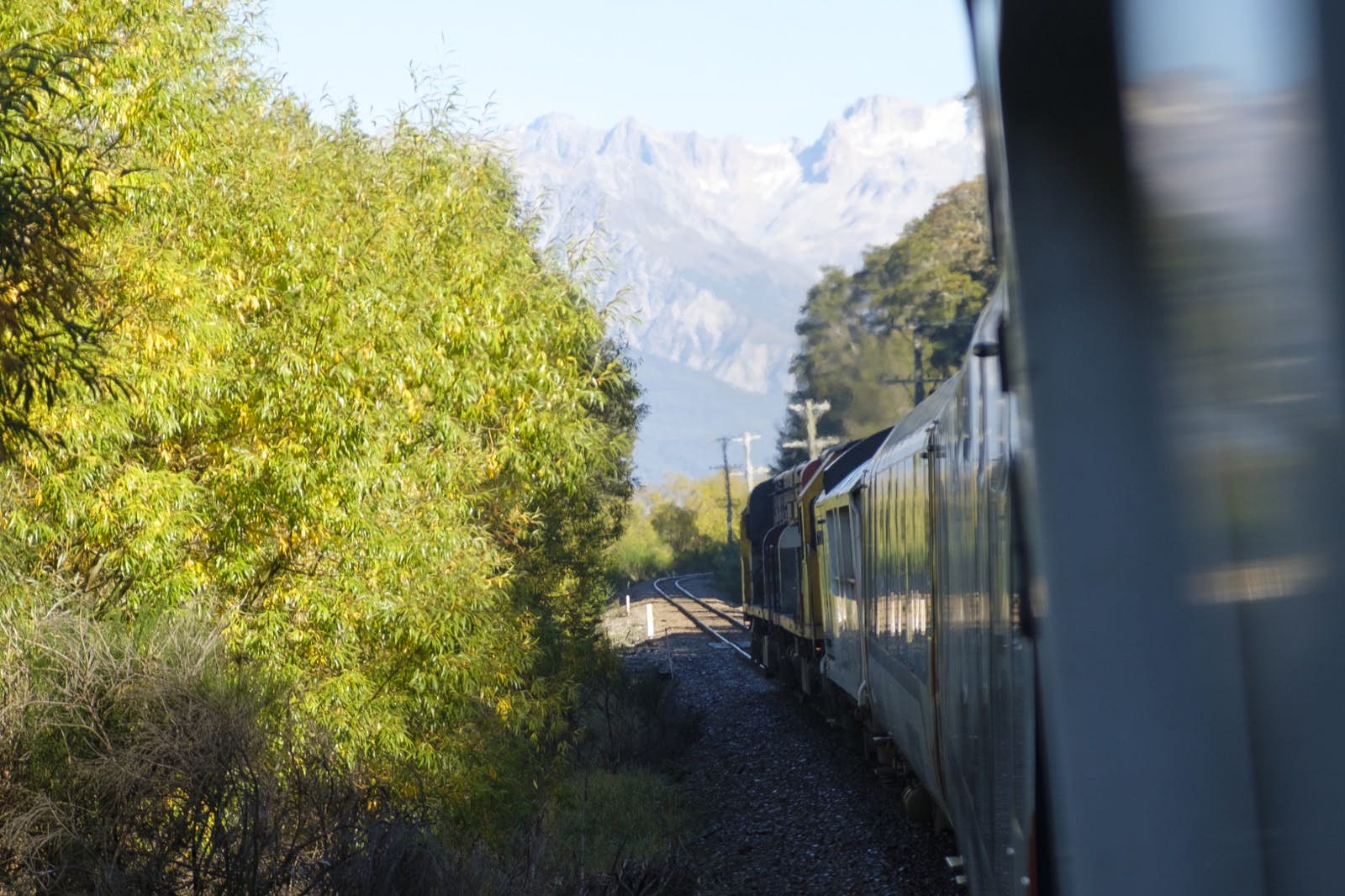 A train rumbles past some brilliant green foliage with rocky mountain outcrops up ahead; Amazing train journeys